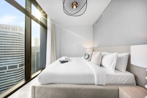 A modern hotel room with a large bed, a view of a cityscape, and a unique ceiling light fixture. - Stayshort - 2 Bedroom in Business Bay Sleeps 6 With Water Canal Views (Dubai)