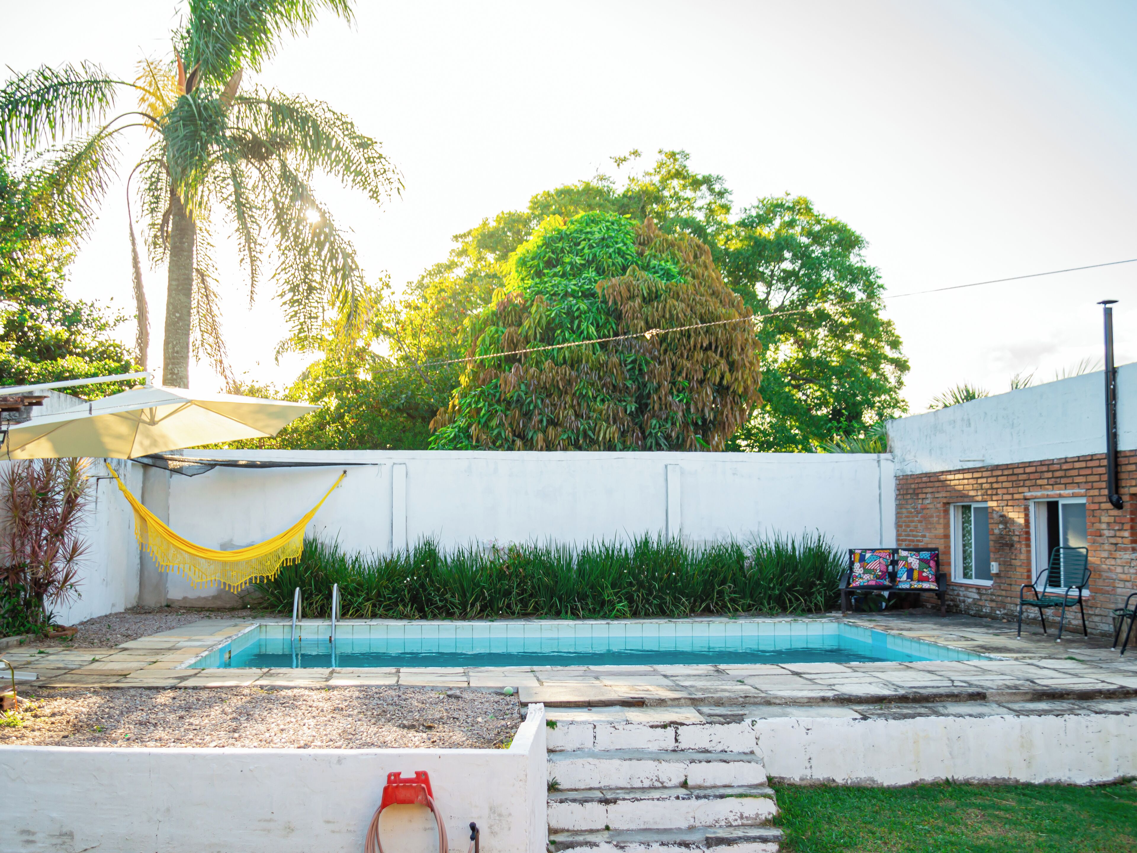 Piscina com parede branca e escadas que descem até a água, cercada por grama e uma rede.