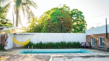 Piscina com parede branca e escadas que descem até a água, cercada por grama e uma rede.