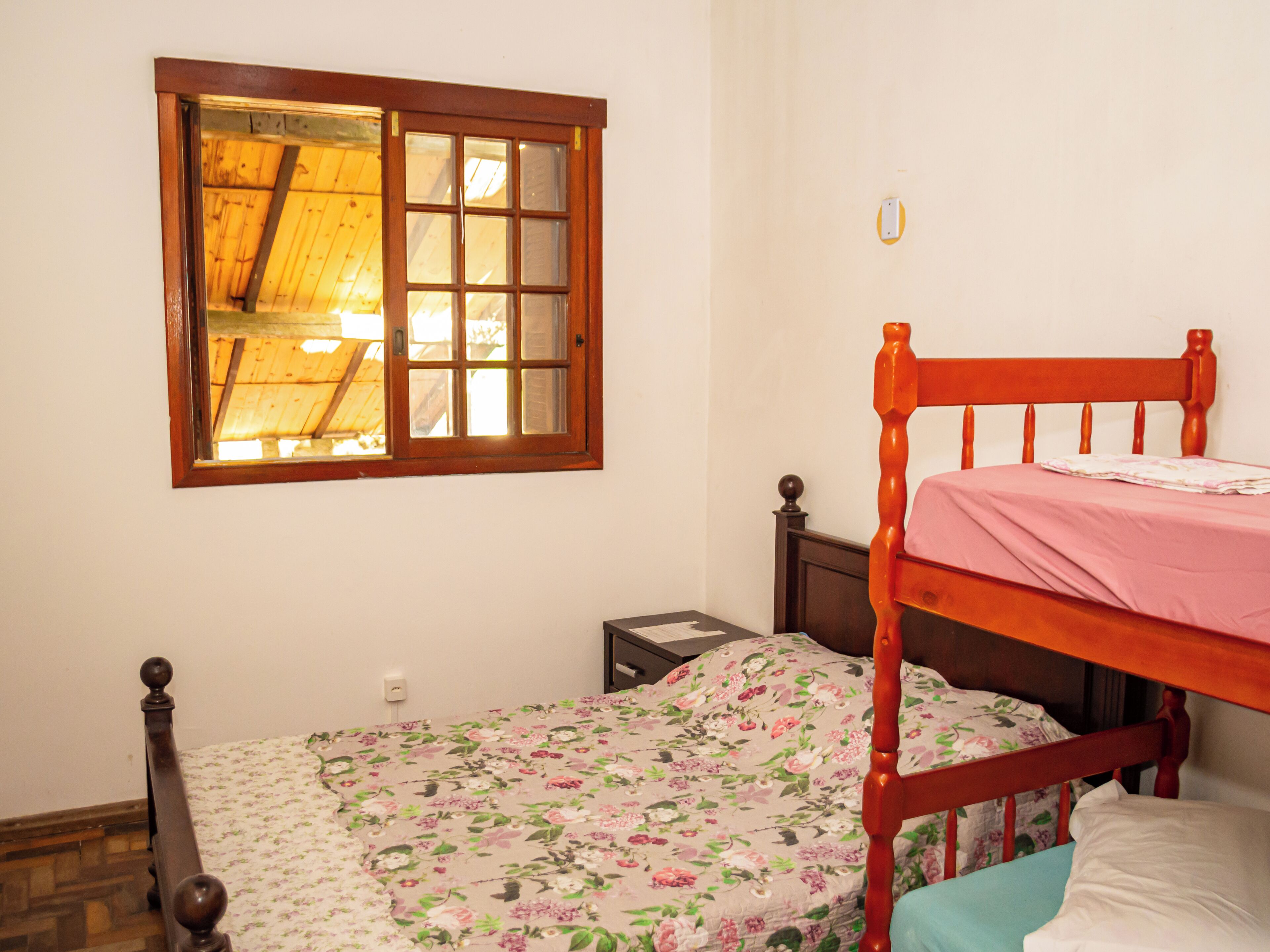 A single bed with a floral bedspread, a wooden headboard, and a window with a wooden frame.