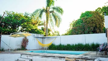 A swimming pool with a hammock, a wooden bench, and a white wall.