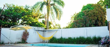 A swimming pool with a hammock, a wooden bench, and a white wall.