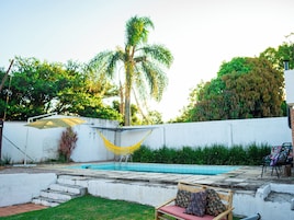 Uma piscina com uma rede, um banco de madeira e uma parede branca.