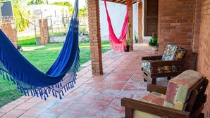 A covered patio with a hammock, wooden furniture, and a brick wall.