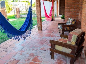 A covered patio with a hammock, wooden furniture, and a brick wall. - pousada santo antonio (Pelotas)