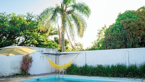 A swimming pool with a hammock, palm trees, and a white wall.