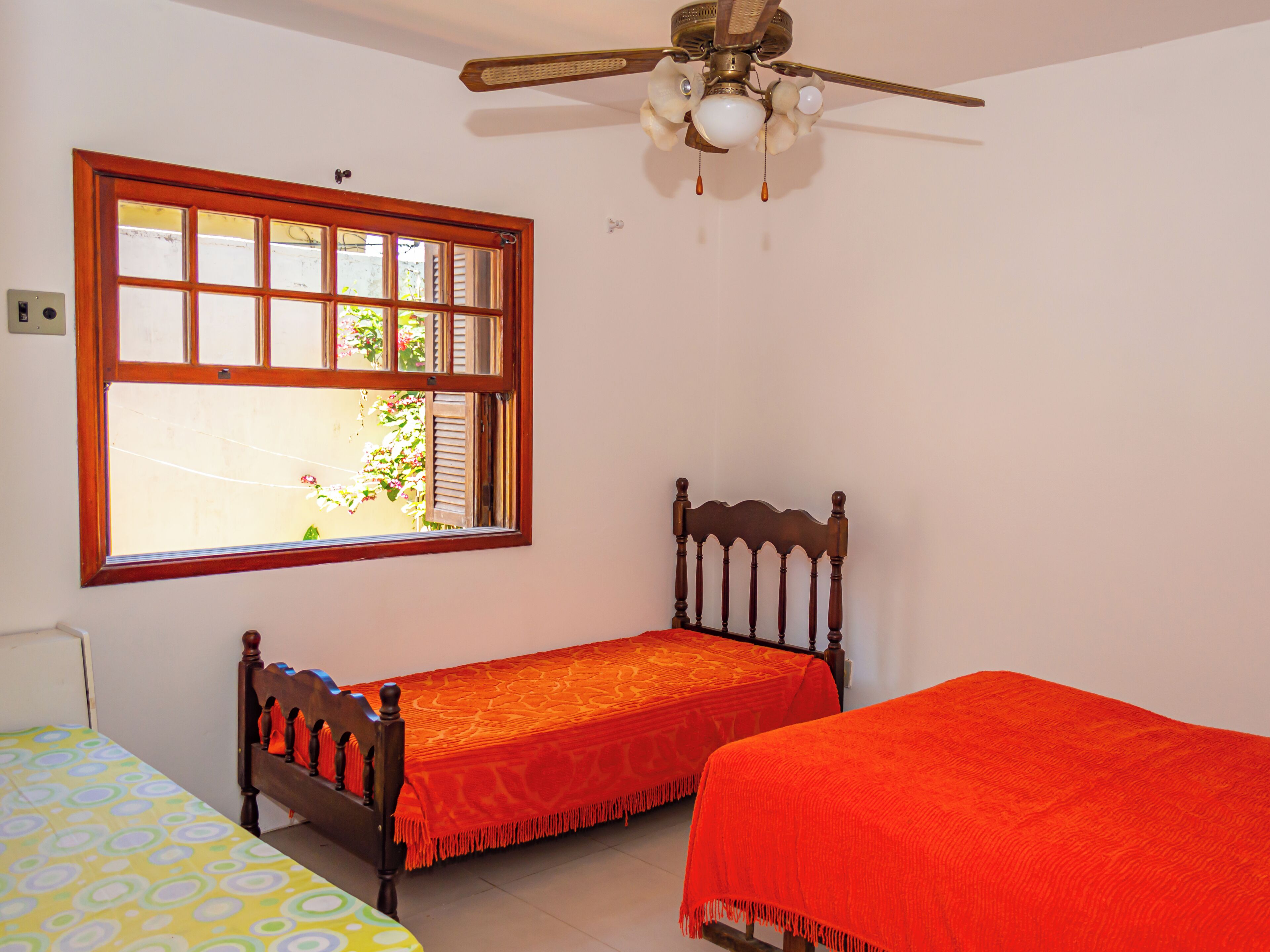 A bedroom with two single beds, a wooden headboard, a ceiling fan, and a window with a view of greenery outside.