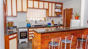 A kitchen with wooden cabinets, a brick island, a gas stove, and a refrigerator. - pousada santo antonio (Pelotas)