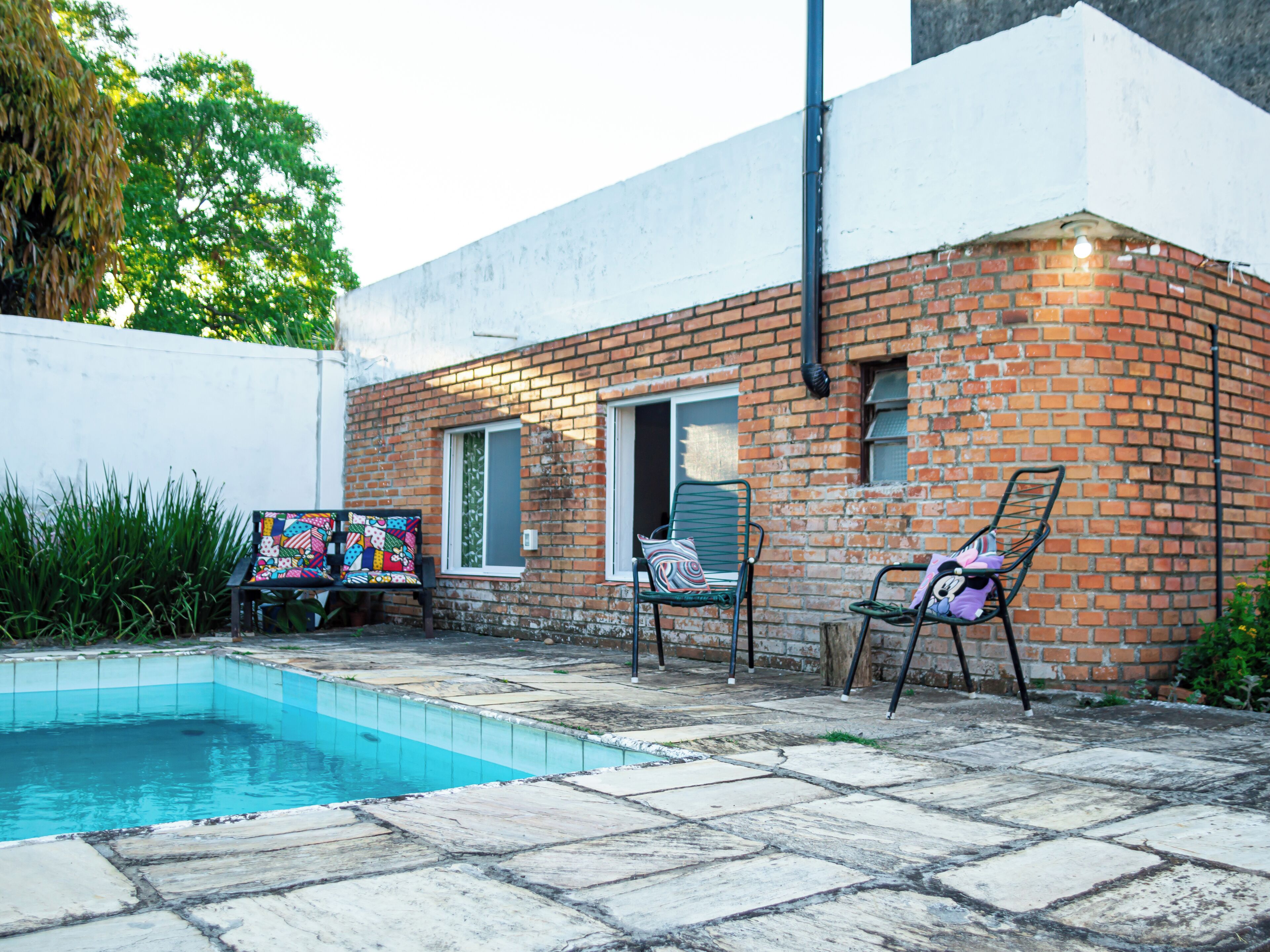 A brick house with a swimming pool, two chairs, and a colorful painting.