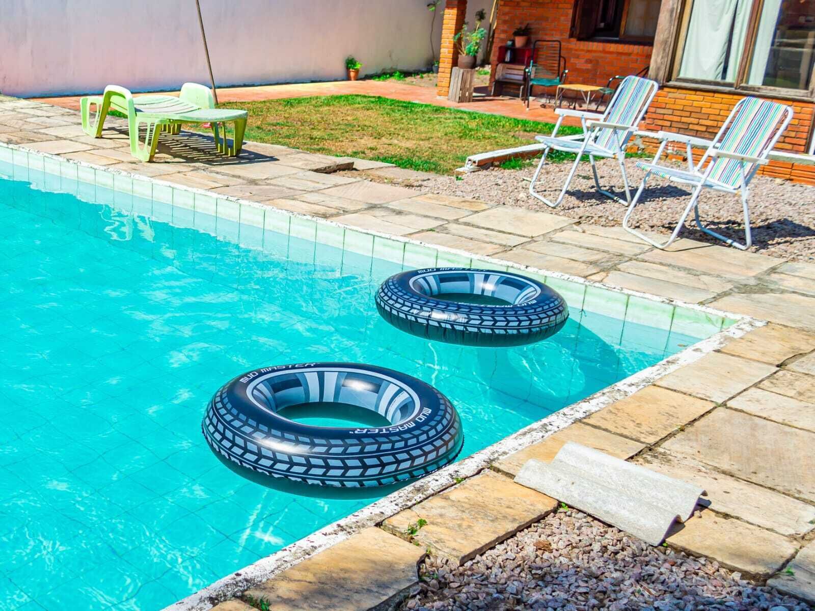 A swimming pool with two inflatable rings, a patio with chairs, and a brick building in the background.
