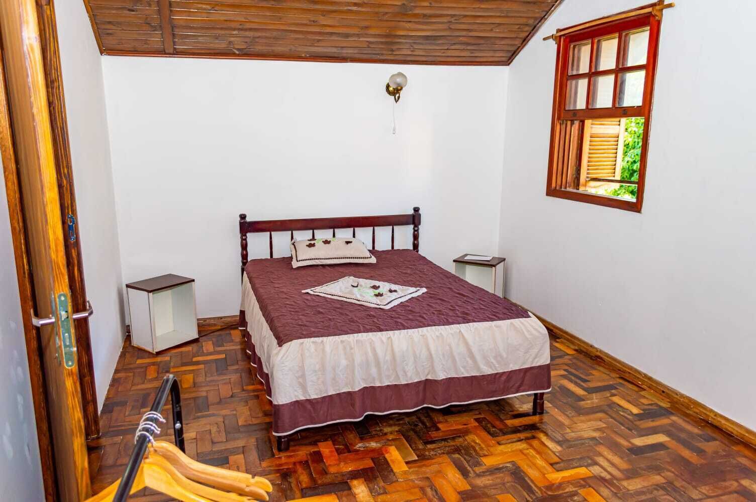 Une chambre avec un lit en bois, une fenêtre donnant sur un paysage verdoyant et un parquet à motifs en chevrons.