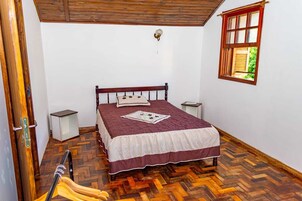 A bedroom with a wooden bed, a window with a view of greenery, and a herringbone-patterned floor.