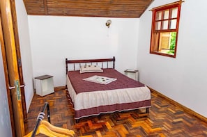 Un dormitorio con una cama de madera, una ventana con vistas a zonas verdes y un suelo con motivo de espiga.
