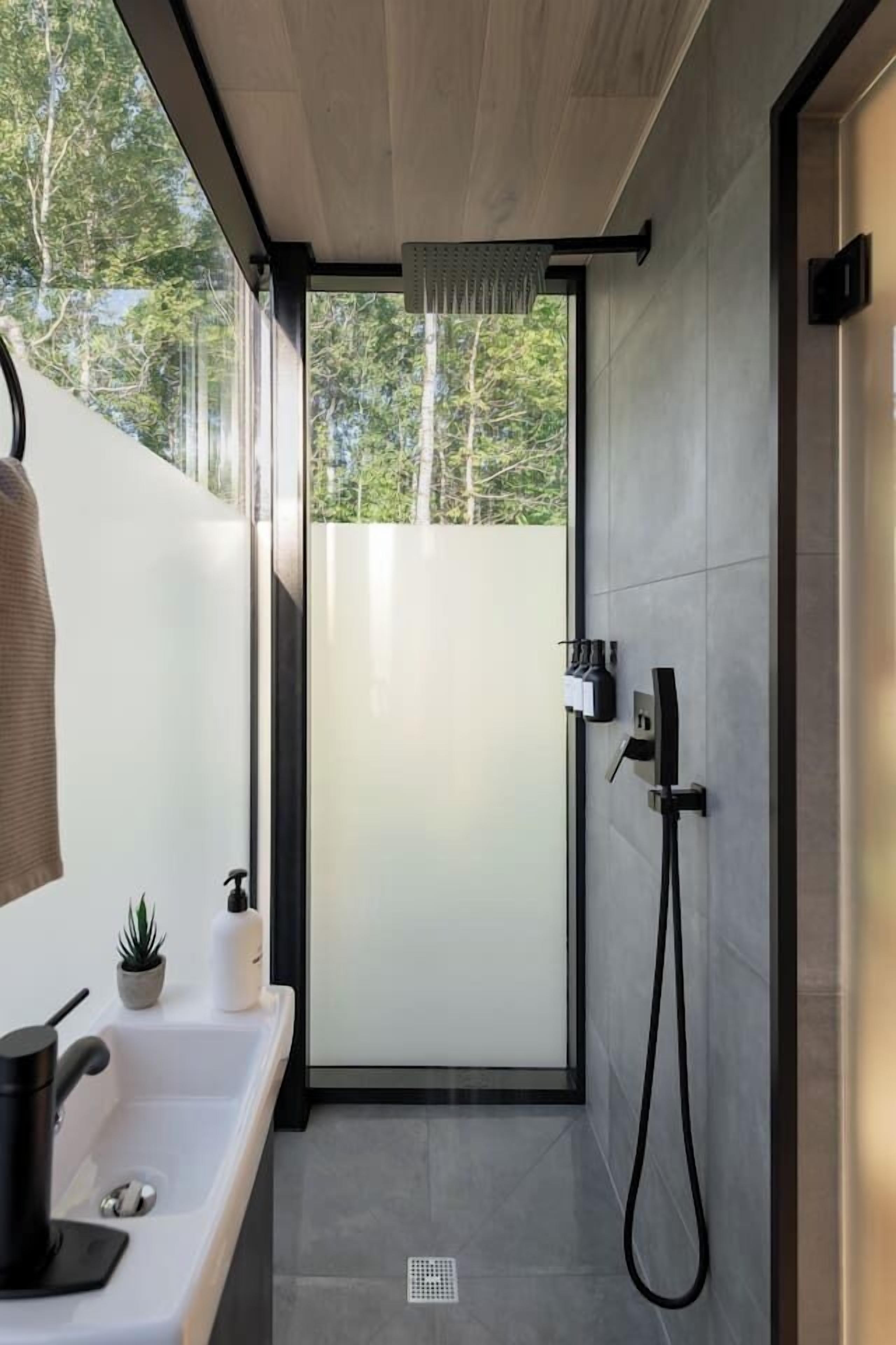 Un baño moderno con ducha, lavamanos, toalla y una planta pequeña.