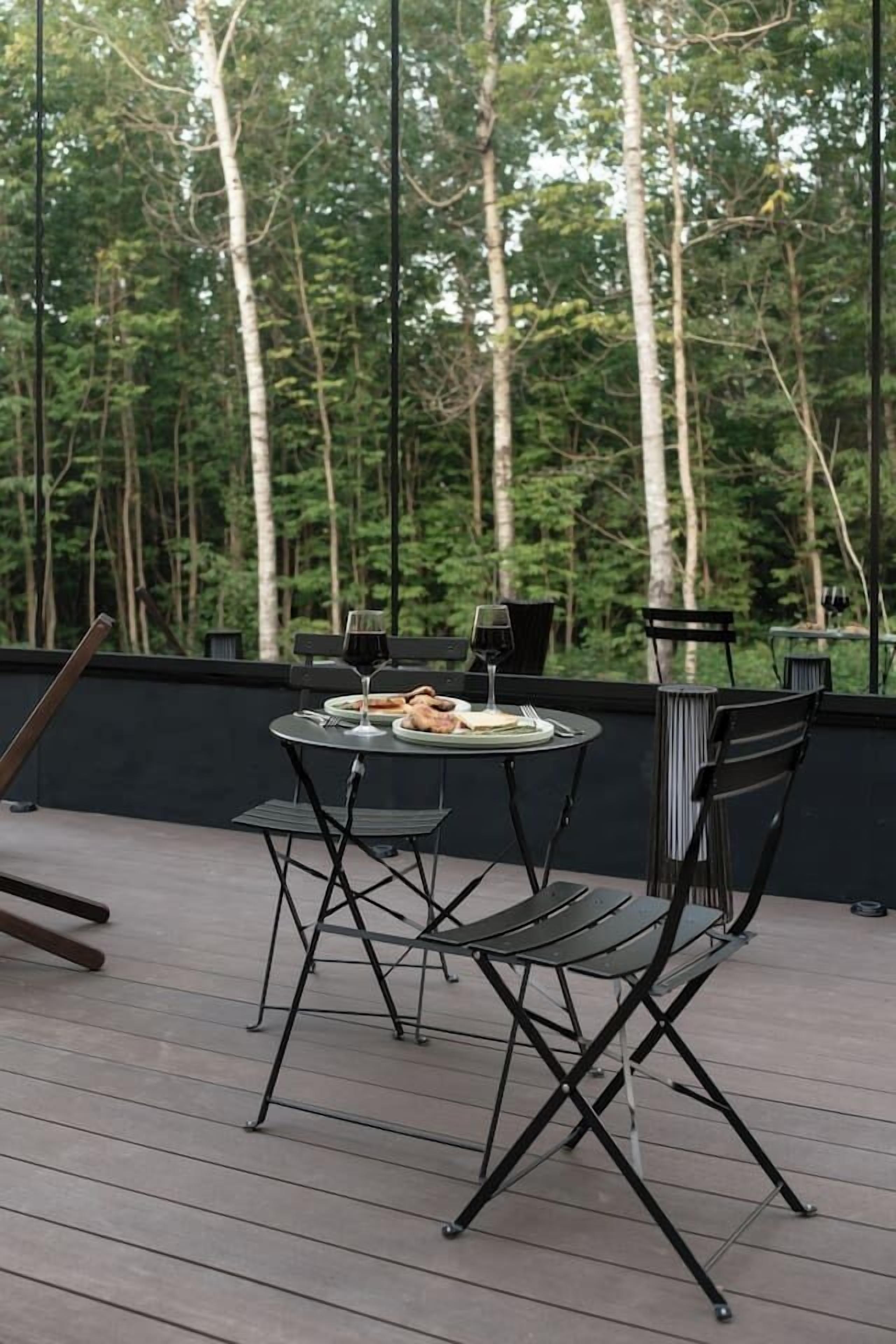 An outdoor dining area with a table and chairs, surrounded by a forested backdrop.