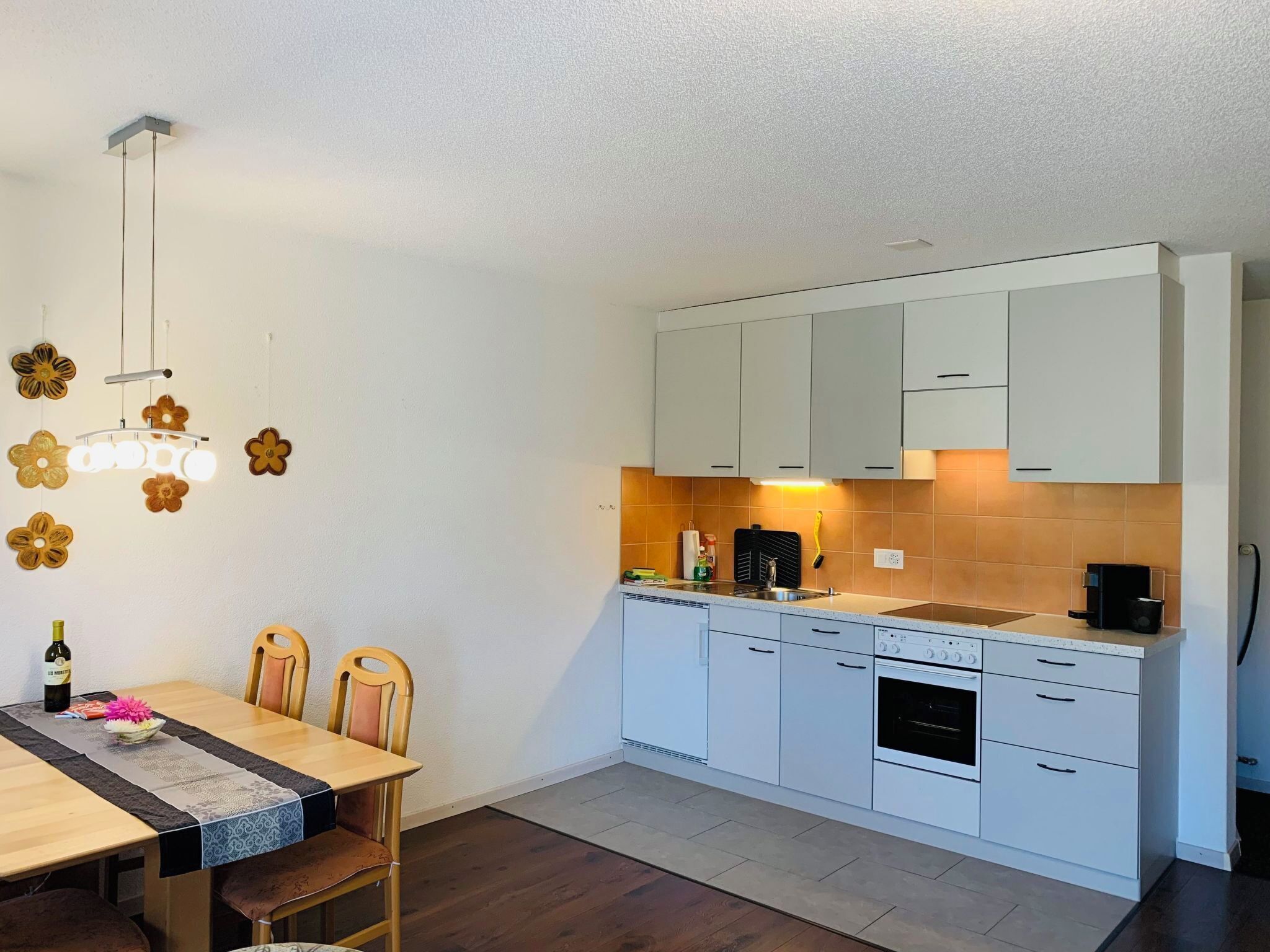 A compact kitchen with white cabinets, a built-in oven, and a dining area with a wooden table and chairs.