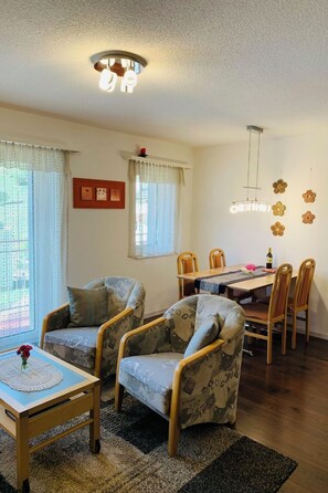 A living room with a dining area, featuring a ceiling light, patterned armchairs, a wooden dining table, and a rug. - Perle "Rinderhoru" # 4-bed apartment, Dusche, WC 4-Bettwohnung, Dusche, WC by Interhome (Leukerbad)