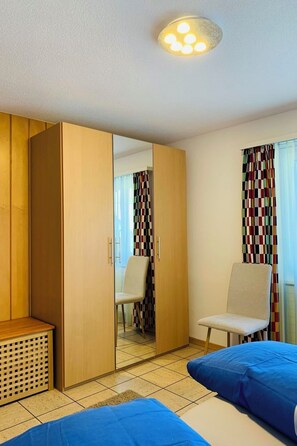 A room with a wardrobe, a chair, and two beds. - Perle "Rinderhoru" # 4-bed apartment, Dusche, WC 4-Bettwohnung, Dusche, WC by Interhome (Leukerbad)