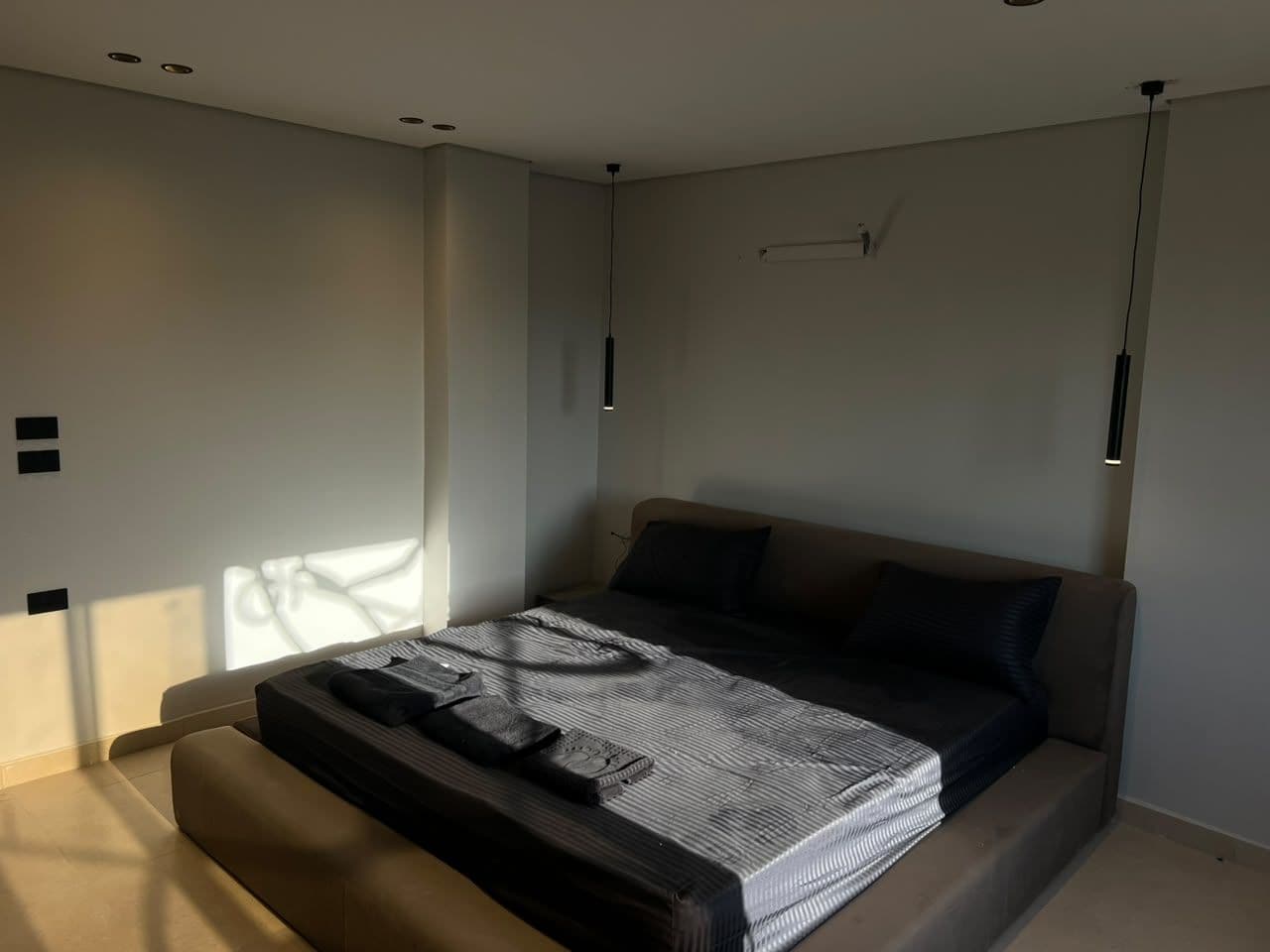 A modern bedroom with a bed, a bedside table, and a hanging light fixture.