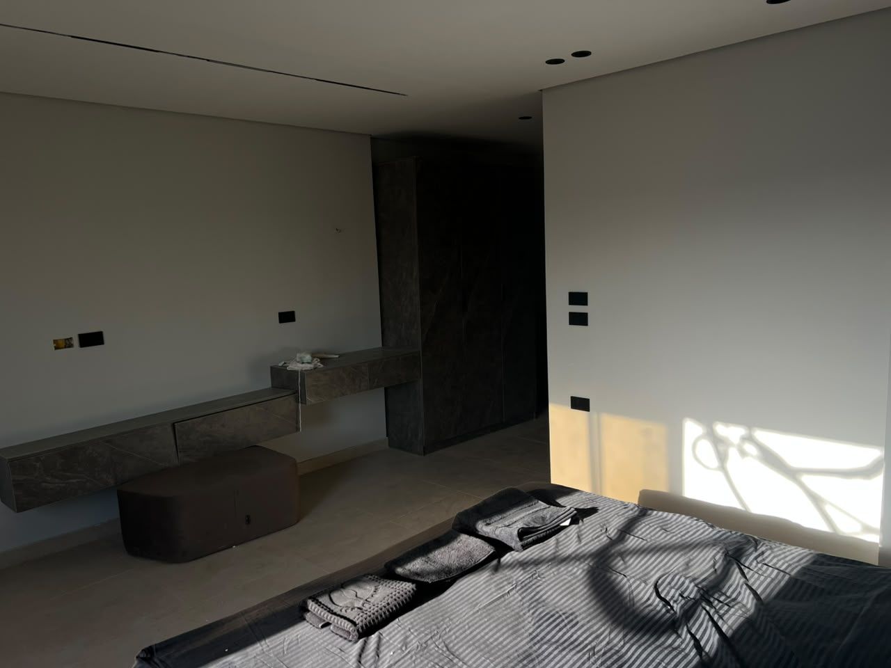 Un dormitorio moderno con cama, banco, una mesita y un banco empotrado a lo largo de la pared.