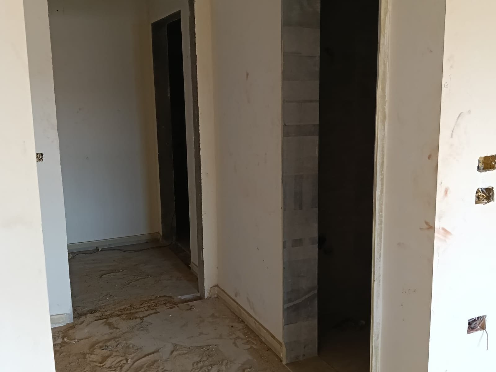 Un pasillo estrecho con piso de baldosas, una puerta a la izquierda y una habitación visiblemente parcial a la derecha.