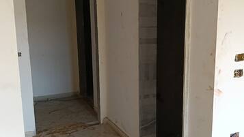 Un pasillo estrecho con piso de baldosas, una puerta a la izquierda y una habitación visiblemente parcial a la derecha.