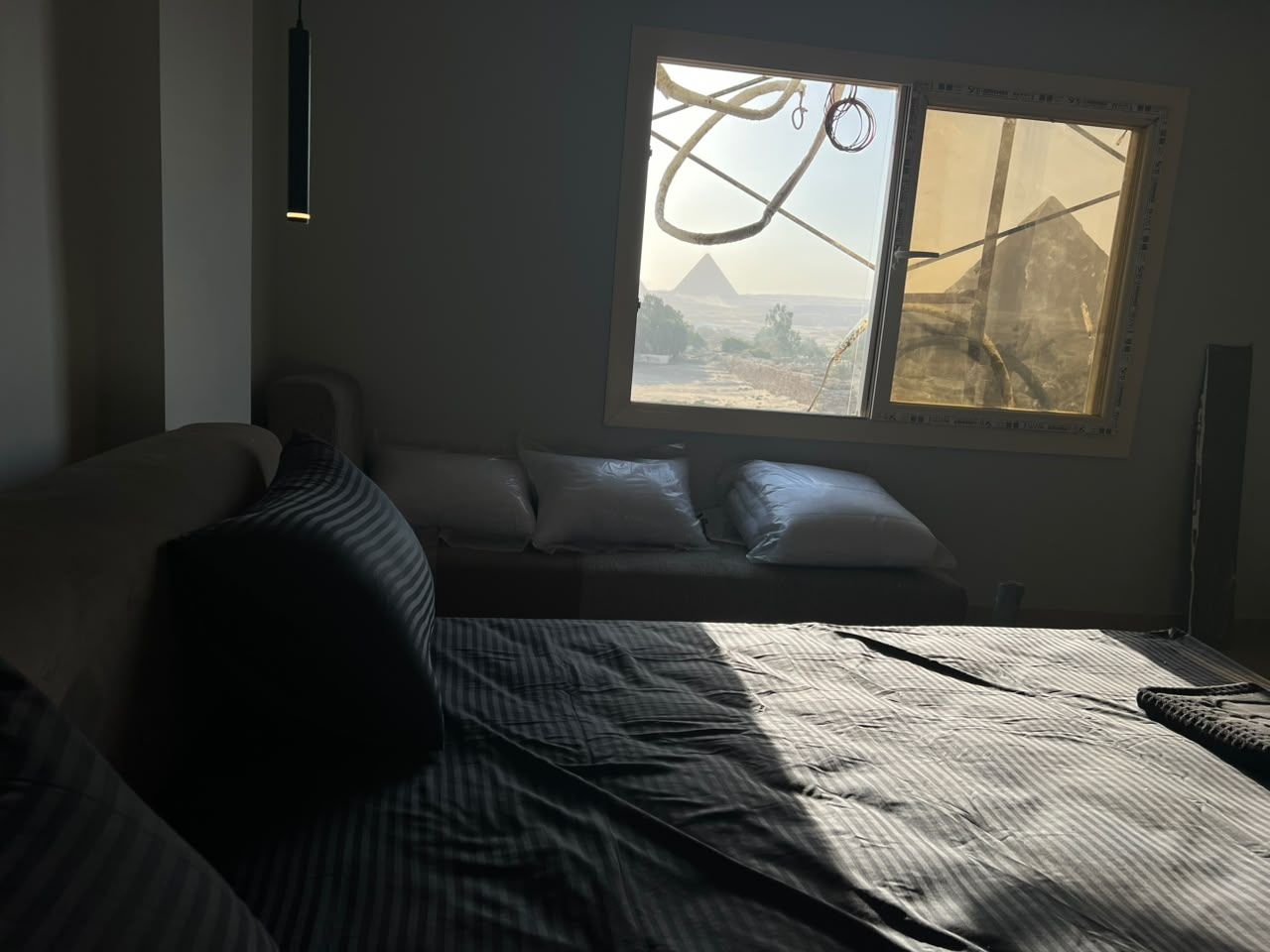 A room with a bed, a window with a view of a mountain, and a hanging light fixture.