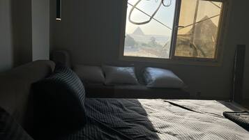 A room with a bed, a window with a view of a mountain, and a hanging light fixture.