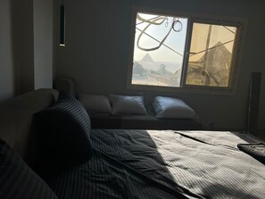 A room with a bed, a window with a view of a mountain, and a hanging light fixture. - Royal Pyramids Land Hotel (Giza)