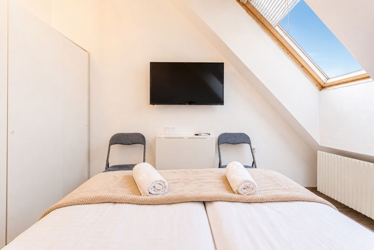 Ett sovrum med en säng, två stolar, en tv och ett takfönster.