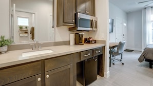 A modern bathroom with a large mirror, dark wooden cabinets, a built-in microwave, and a coffee station. - Work + Unwind Poolside! Nurse-ready Houston Rental (Houston)