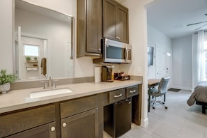 A modern bathroom with a large mirror, dark wooden cabinets, a built-in microwave, and a coffee station. - Work + Unwind Poolside! Nurse-ready Houston Rental (Houston)