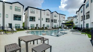 A modern residential building with a swimming pool, outdoor seating, and a clear sky. - Work + Unwind Poolside! Nurse-ready Houston Rental (Houston)