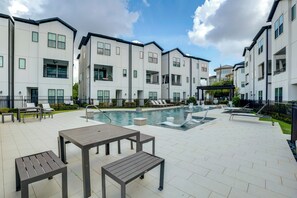 A modern residential building with a swimming pool, outdoor seating, and a clear sky. - Work + Unwind Poolside! Nurse-ready Houston Rental (Houston)