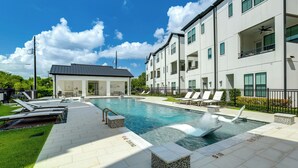 A modern pool area with lounge chairs, a small building, and a multi-story residential building with balconies. - Work + Unwind Poolside! Nurse-ready Houston Rental (Houston)