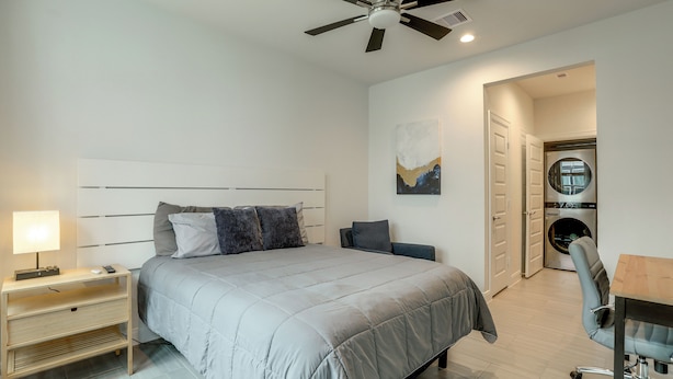 A bedroom with a bed, bedside table, lamp, and a ceiling fan. - Work + Unwind Poolside! Nurse-ready Houston Rental (Houston)