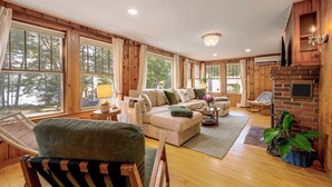 A cozy living room with a sofa, armchairs, a fireplace, and large windows.