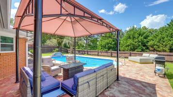 A backyard with a covered seating area, a swimming pool, and a barbecue grill.