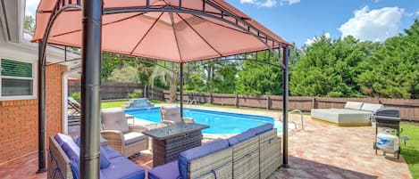Un patio trasero con una zona de estar techada, una piscina y una parrilla.