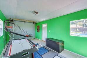 A room with a pool table, a ceiling fan, a poster on the wall, and a window with a view of a house and trees. - Poolside Paradise w/ Game Room! Prattville Getaway (Prattville)