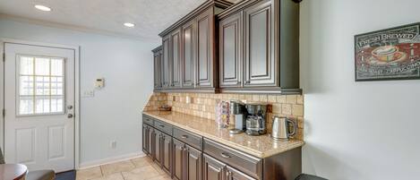 A kitchen with dark wooden cabinets, a countertop with a coffee maker, and a trash can.