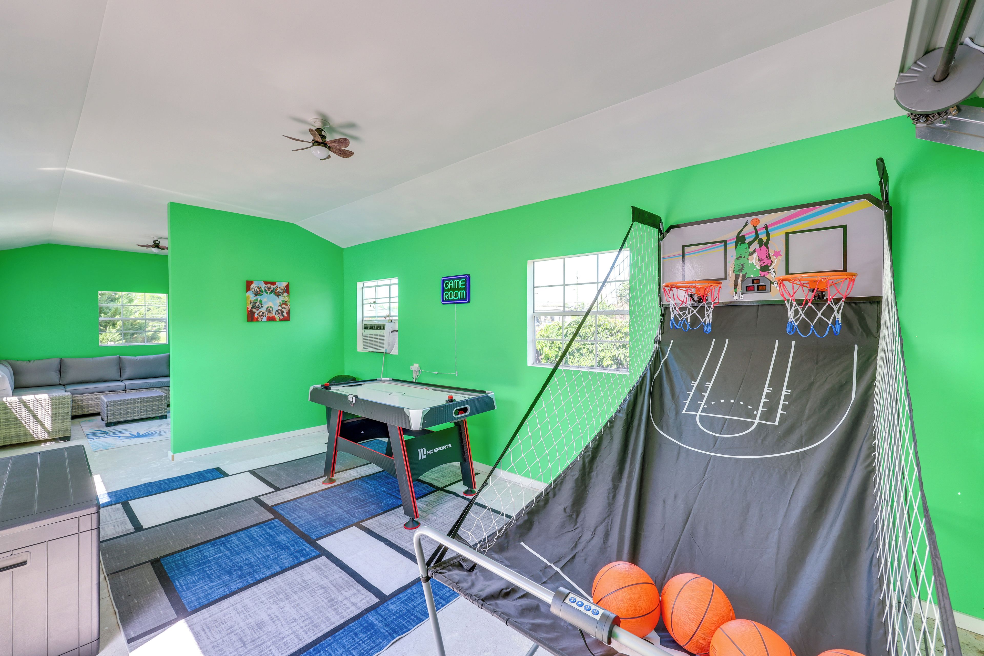 A room with green walls, a pool table, a basketball hoop, and a sofa.