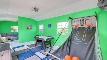 Una habitación con paredes verdes, mesa de billar, aro de baloncesto y sofá.