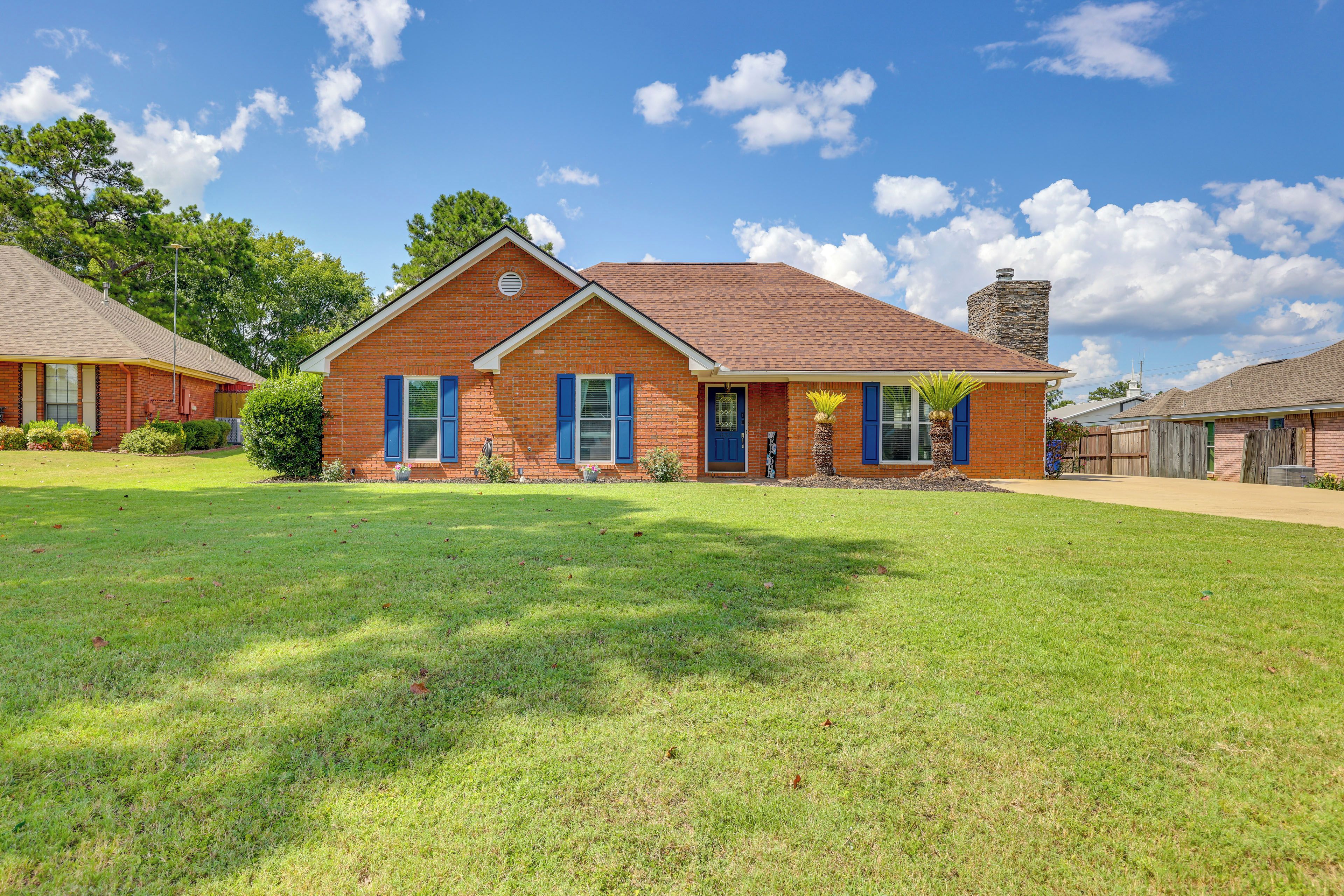 A two-story brick house with a front lawn, a stone chimney, and a clear blue sky.