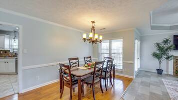 A dining area with a wooden table and chairs, a chandelier, and a potted plant.