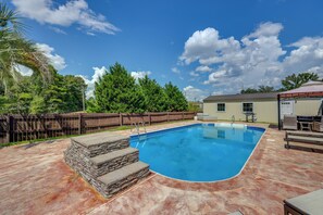 A swimming pool with a stone border, a wooden fence, and a covered barbecue area. - Poolside Paradise w/ Game Room! Prattville Getaway (Prattville)