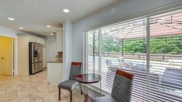 A kitchen with a stainless steel refrigerator, a dining area with two chairs and a table, and a large window with blinds.