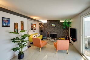 A living room with a stone fireplace, a yellow sofa, orange chairs, and a large potted plant.
