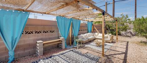Un espacio de estar al aire libre techado con alfombra estampada, un sofá y un banco.