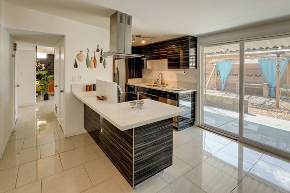 A modern kitchen with a central island, a built-in oven, and a large window with a view of the outdoors.